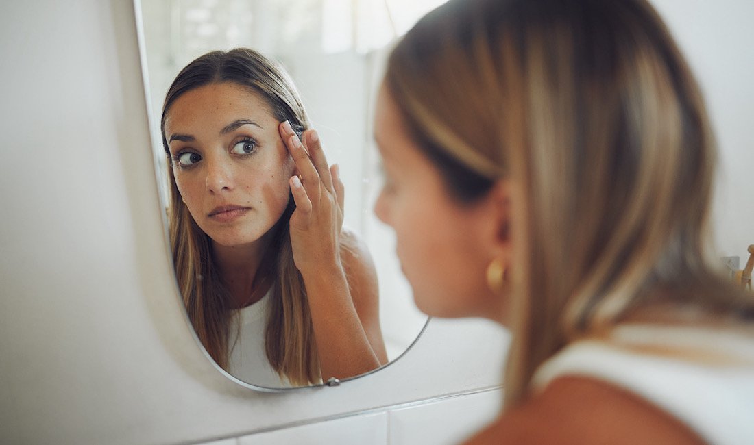 Woman looking in the mirror checking her skin for hyperpigmentation.